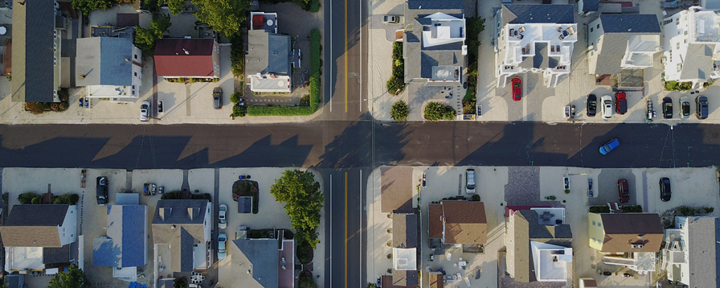 Aerial view of a residential street intersection with houses and parked cars casting long shadows during sunrise or sunset.