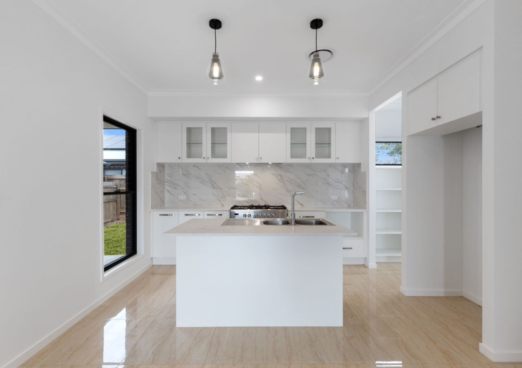 Modern kitchen interior with white cabinetry and marble countertops, featuring a central island and pendant lighting.