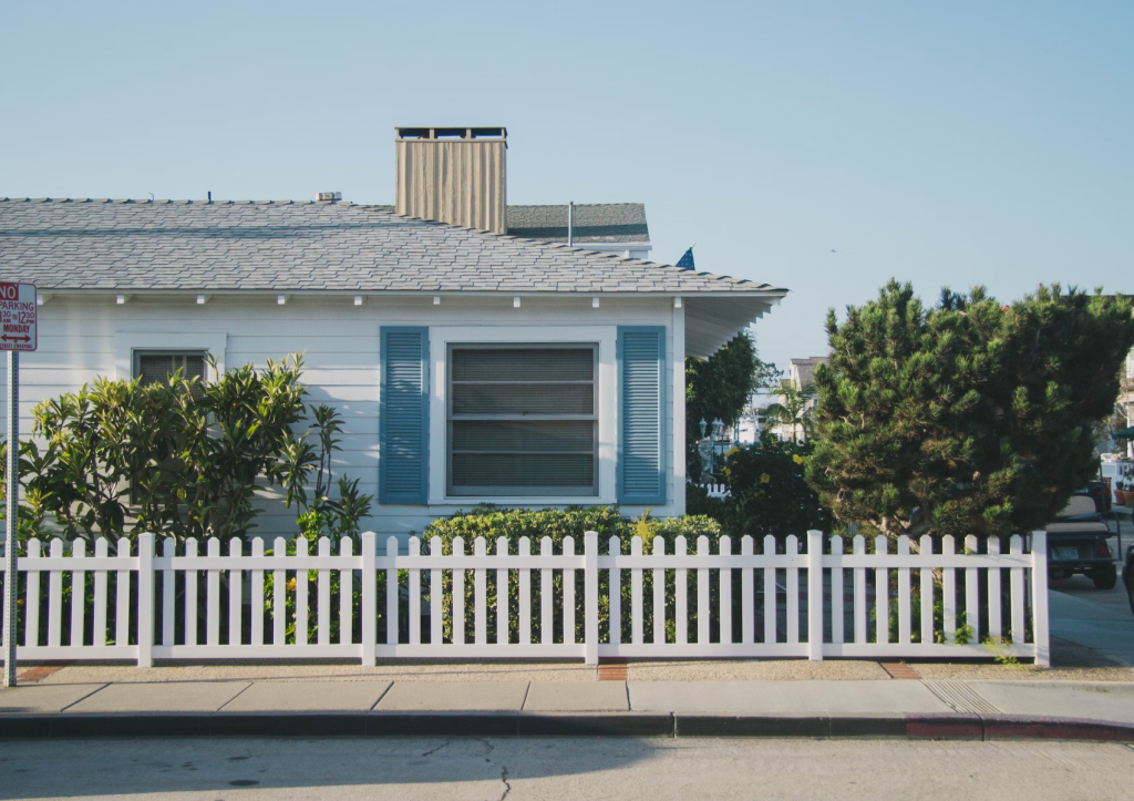 A single-story house with a white picket fence and blue shutters on a sunny day.