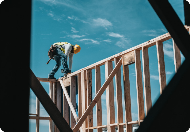 Construction worker inspecting wooden framework at a Buildertrend construction site under a clear blue sky.