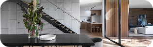 A modern dining area featuring a dark table and a vase of flowers, seamlessly blending into the custom home's open layout. Visible staircase, open kitchen, and living room with wooden accents and large glass doors complete the sophisticated design.