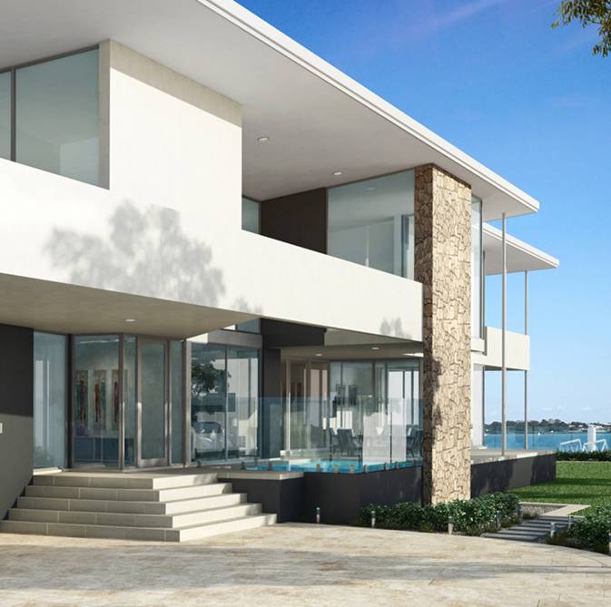 A modern custom home boasting large windows, stone accents, and steps leading to the entrance. It's beautifully surrounded by lush greenery and overlooks a tranquil body of water under a clear blue sky.